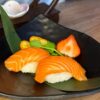 Exquisite Nigiri Salmon served on a dark, textured plate, complemented by fresh strawberries and kumquats