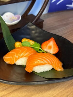 Exquisite Nigiri Salmon served on a dark, textured plate, complemented by fresh strawberries and kumquats