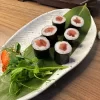 Fresh-Maki-Salmon-sushi-snack-from-Edinburgh-served-on-a-leaf-on-a-white-plate-with-nori-wrap Six pieces of tuna maki sushi rest on a leaf-lined ceramic plate, elegantly garnished with greens and a small orange accent, capturing the essence of Edinburgh's culinary scene.