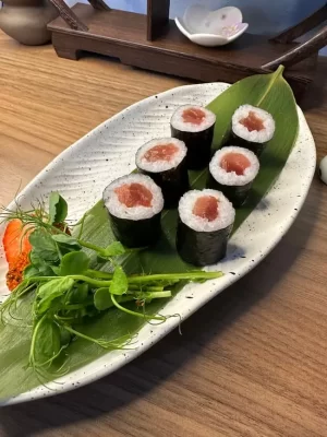 Six pieces of tuna maki sushi rest on a leaf-lined ceramic plate, elegantly garnished with greens and a small orange accent, capturing the essence of Edinburgh's culinary scene.