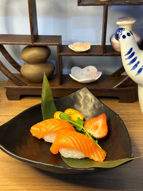 Nigiri Salmon on a black plate with a green leaf and vibrant garnish - a taste of Japan in every bite.