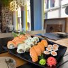 A black plate with Salmon Lover Sushi set on a wooden table in a brightly lit restaurant.