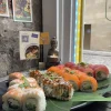 A platter from the Sushi Set 2 rests on a banana leaf, evoking the charm of an Edinburgh street market. In the background, a candle and Buddha statue accompany postcards on a brick wall, enhancing the serene ambiance.