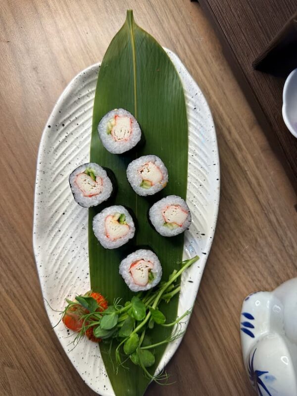 Top view of Maki Crab sushi in Edinburgh with garnish on a white plate and wooden shelf backdrop.