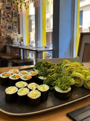The Vegan set, featuring assorted rolls and seaweed salad, is presented on a wooden table in a modern, well-lit restaurant.