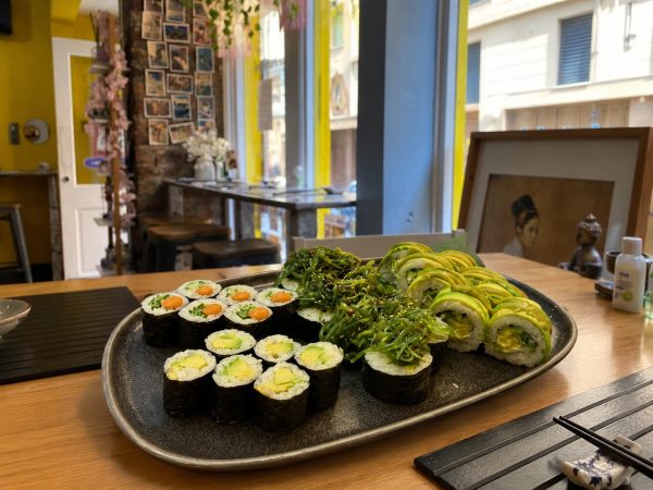 The Vegan set, featuring assorted rolls and seaweed salad, is presented on a wooden table in a modern, well-lit restaurant.