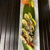 Sushi rolls with sesame seeds served on a black plate, with ginger on the side, in front of a yellow wall with decorative items