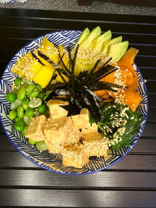 Detailed presentation of Vegan Poke with layers of tofu, mango slices, and avocado cubes, garnished with nori and a drizzle of spicy mayo in Edinburgh