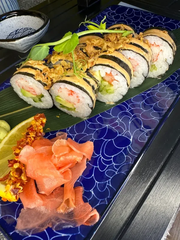 A blue plate of Futomaki crab sushi rolls garnished with a slice of lemon, pickled ginger, and wasabi.