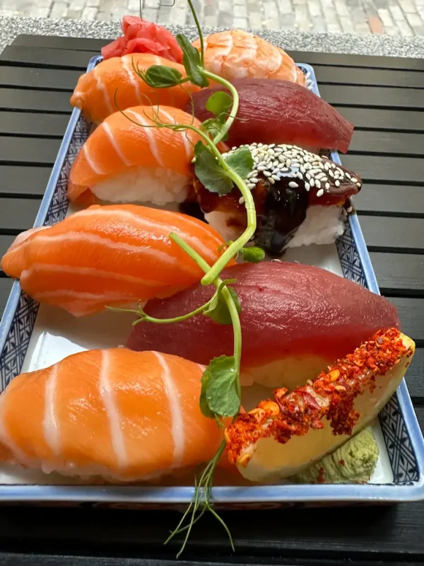 Full view of assorted nigiri sushi set, artistically arranged on a blue plate against an Edinburgh street backdrop