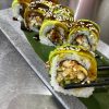 Sushi rolls with sesame seeds served on a black plate, with ginger on the side, in front of a yellow wall with decorative items.