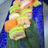 Princes Street Sushi Roll arrayed on a bamboo leaf, showcasing layers of salmon, shrimp, avocado, and mamenori, with tobiko accents, set against a blue ceramic plate background.