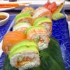 Close-up of Princes Street Sushi Roll with avocado and salmon on top, mamenori wrap, filled with shrimp, soft cheese, and tobiko, presented on a leaf over a blue plate.