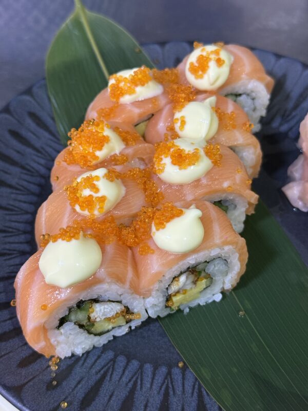 Roter Drache-Rolle: Sushi-Rollen mit Lachs, Sahnesauce und Orangenrogen, serviert auf einem grünen Blatt.