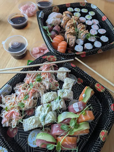 The Imperial feast set features two trays of assorted sushi rolls, sashimi, wasabi, ginger, soy sauce, and chopsticks on a wooden table.