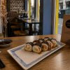 A plate of Futomaki Crab Sweet Chili sushi rolls sits on a wooden table with a menu, soy sauce, and chopsticks nearby.