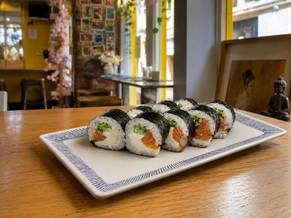 A rectangular plate with eight Futomaki Salmon Phila sushi rolls on a wooden table in a restaurant.
