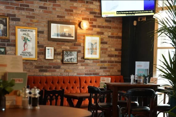 image_2025-08-04_112739895 A cozy restaurant interior with brick walls, framed art, and a tufted orange bench—perfect for enjoying Edinburgh Festival Fringe food.