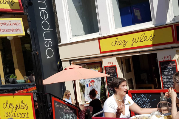 image_2025-08-04_114704932 Two people enjoy food and conversation at Chez Jules during the Edinburgh Festival Fringe, surrounded by French and English signs.
